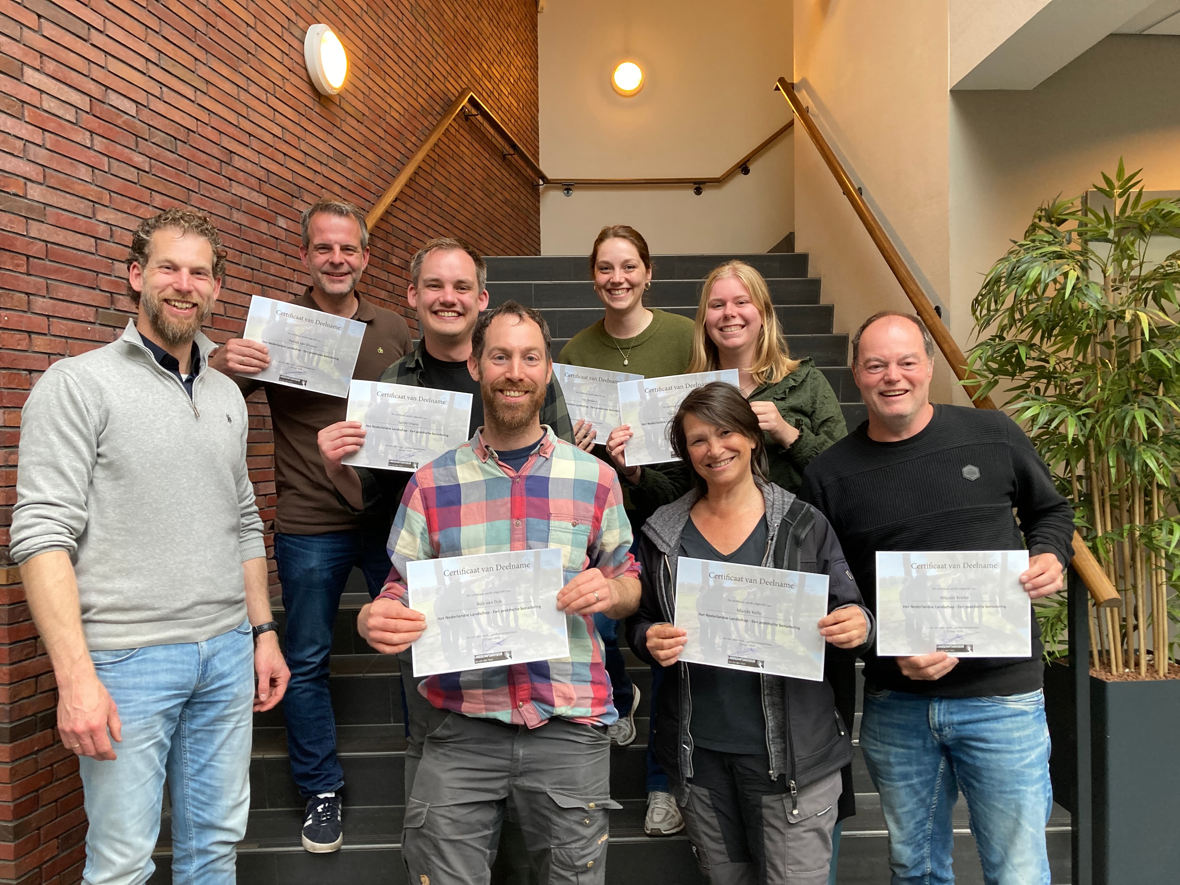 De cursusgroep poseert op een trap met certificaten van deelname.